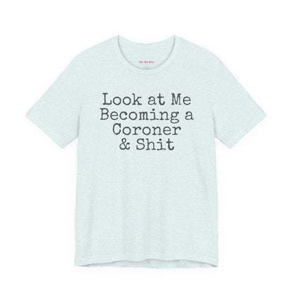 Ice Blue funny coroner T-shirt featuring the phrase Look at Me Becoming a Coroner & Shit in vintage typewriter-style lettering.