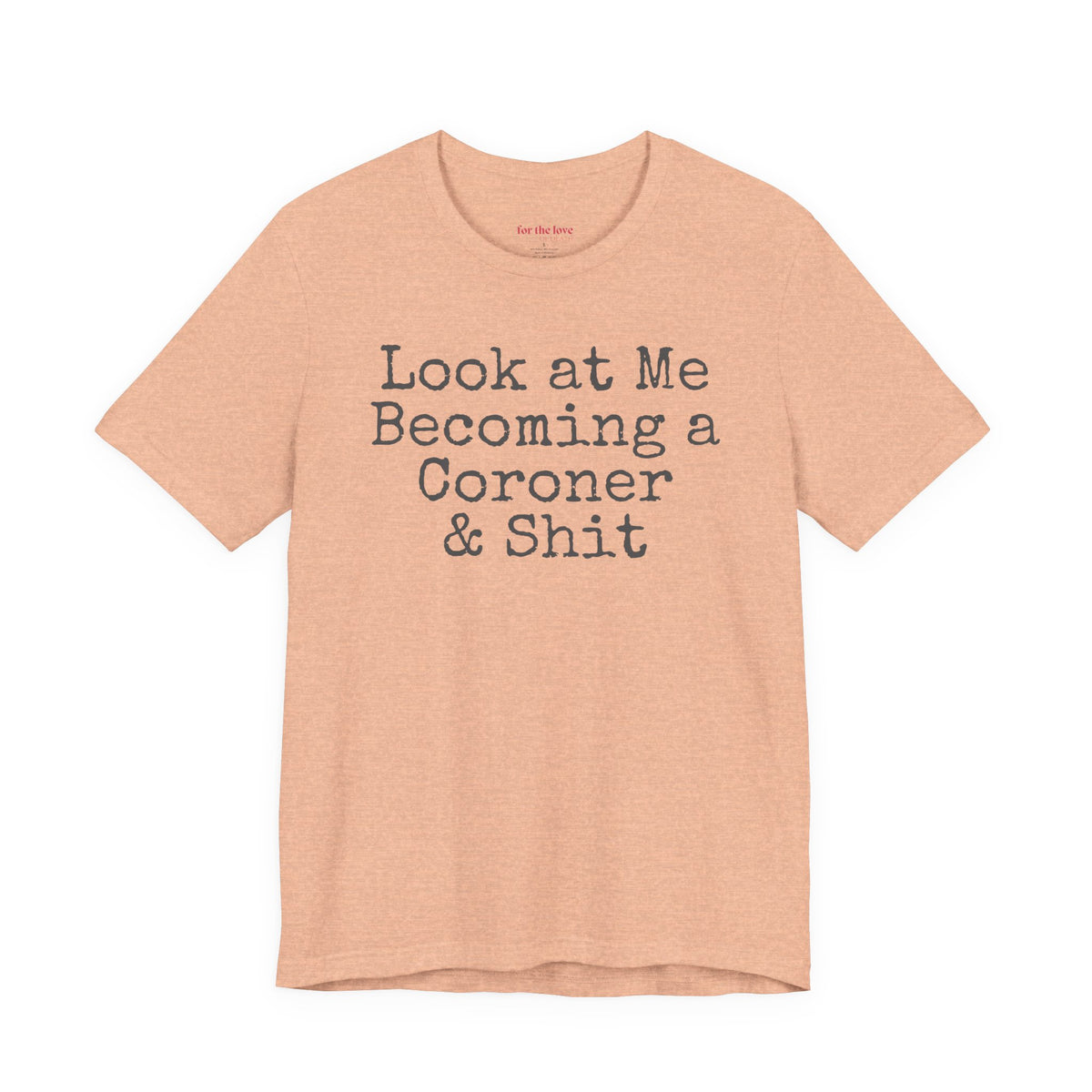 Peach funny coroner T-shirt featuring the phrase Look at Me Becoming a Coroner & Shit in vintage typewriter-style lettering.