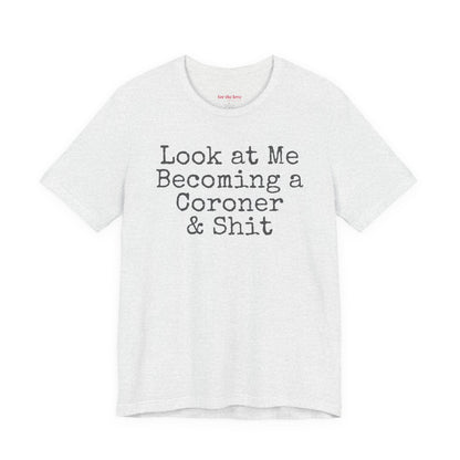 funny coroner T-shirt featuring the phrase Look at Me Becoming a Coroner & Shit in vintage typewriter-style lettering. Ash