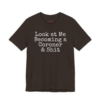 Brown funny coroner T-shirt featuring the phrase Look at Me Becoming a Coroner & Shit in vintage typewriter-style lettering.