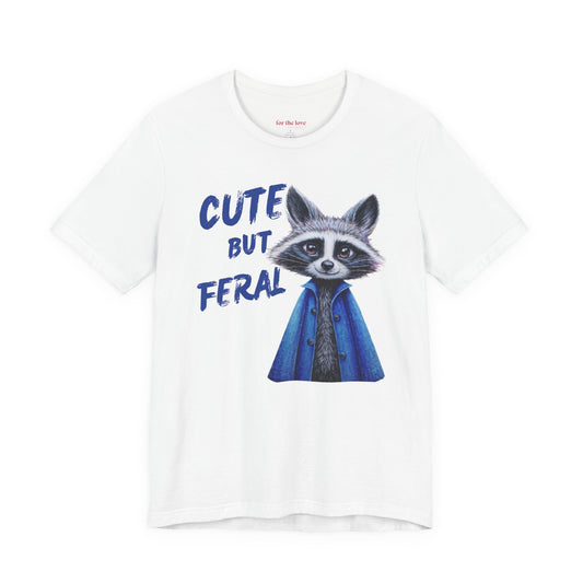 white graphic t-shirt featuring a cute raccoon in a blue coat with the phrase “Cute But Feral”